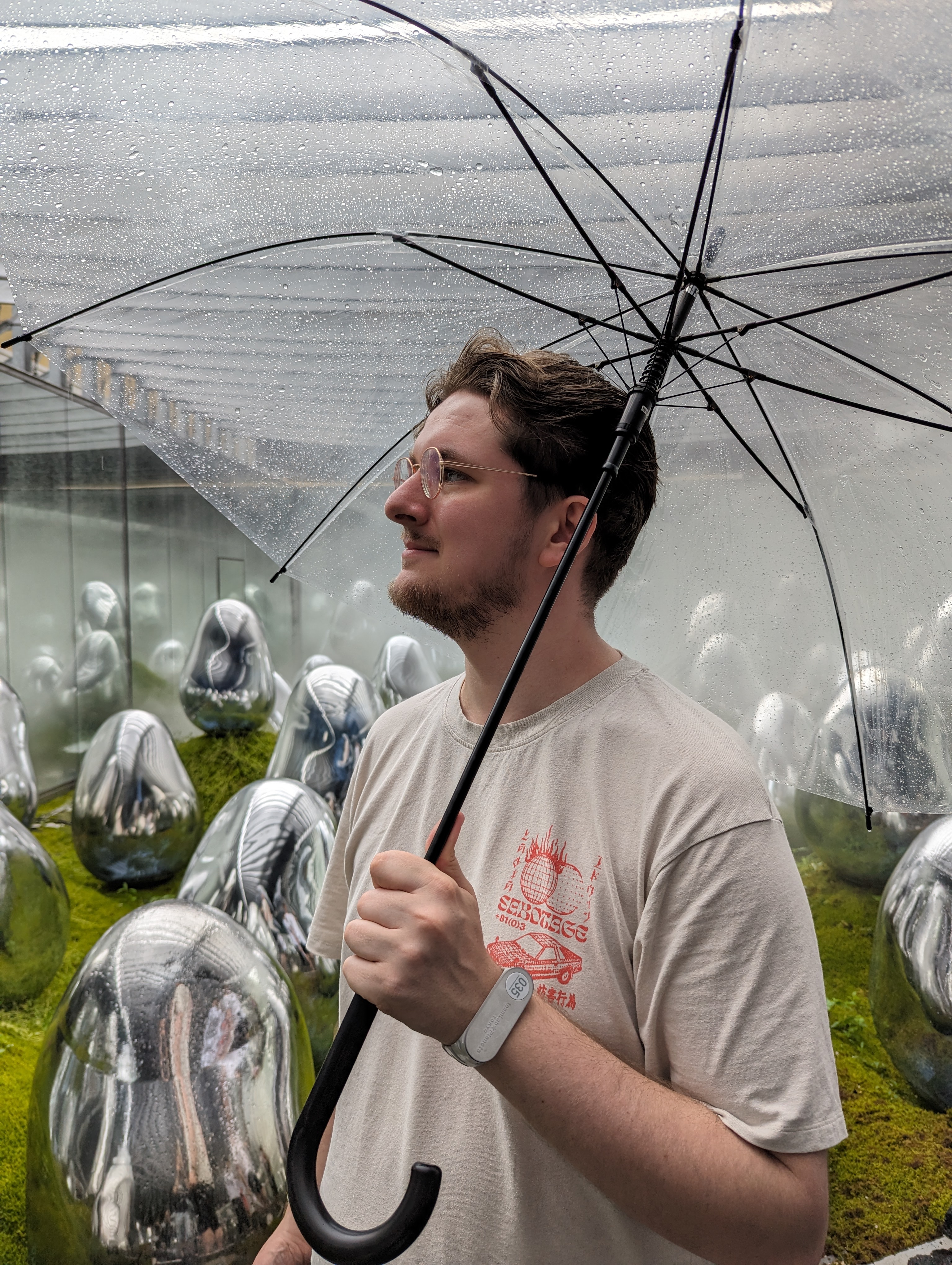 a handsome young man, looking to the left, holding a transparent umbrella