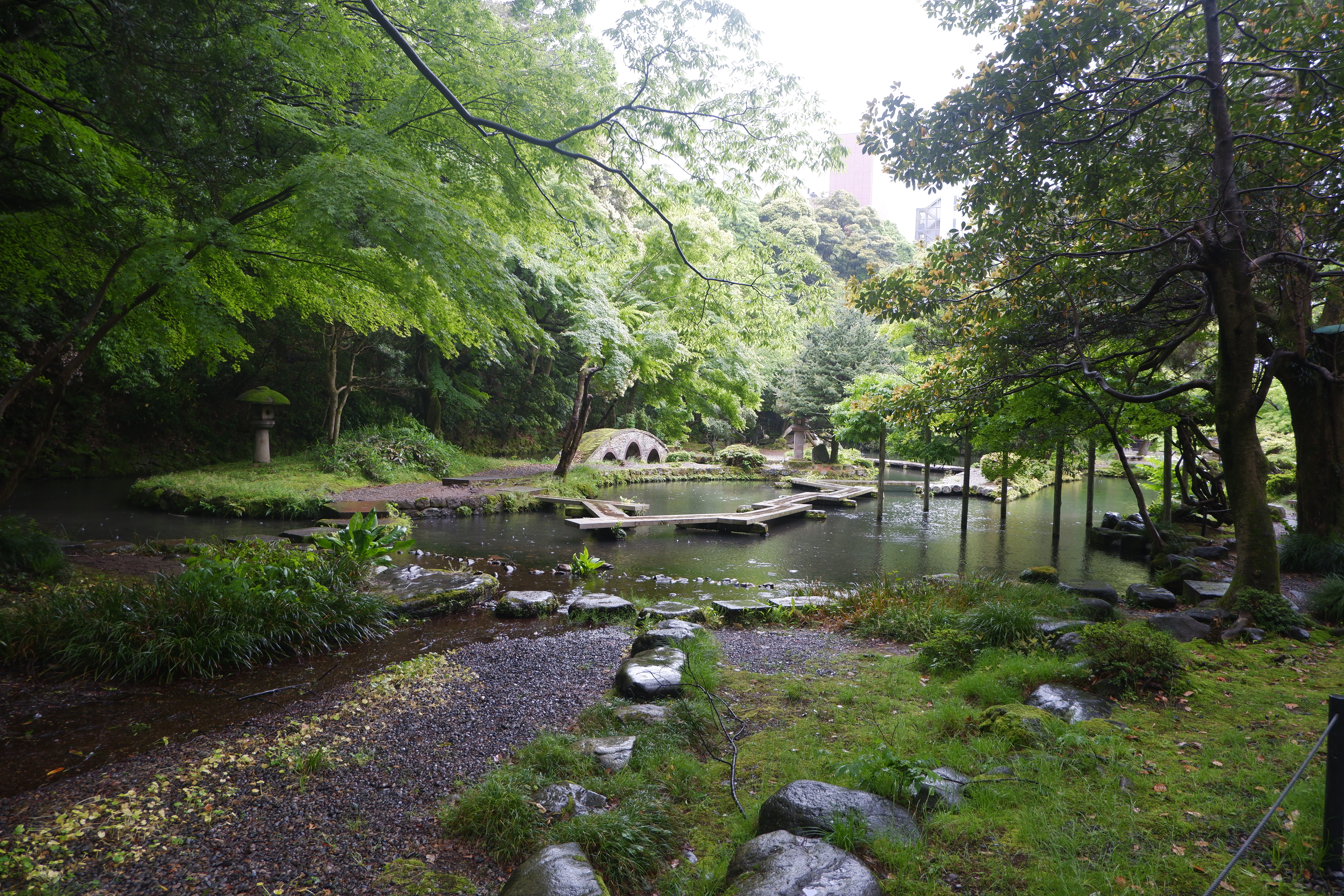 a pond with a stone bridge in a japanese garden with skyscrapers in the far background